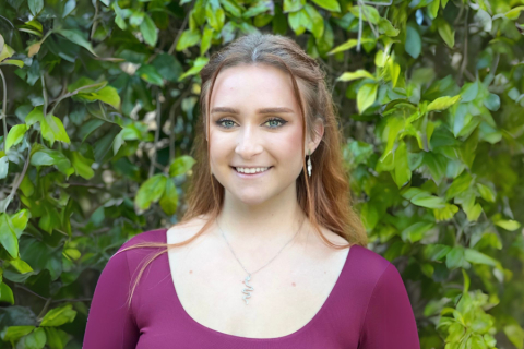 Portrait of person in maroon shirt in front of greenery