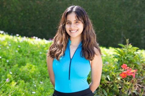 Image of smiling young woman standing in front of a wall with vines covering it